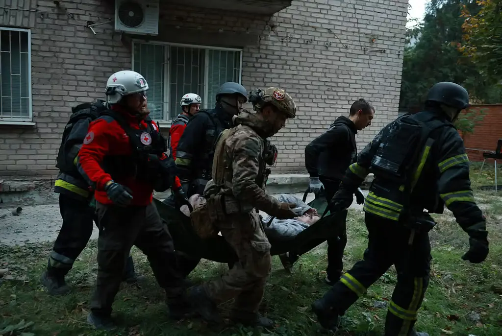 Räddningsarbetare i Zaporizjzja för bort en skadad kvinna efter en rysk attack mot ett flerfamiljshus i helgen.