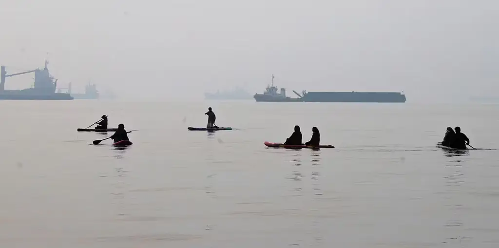 Människor paddlar på sup-brädor i Hormuzsundet utanför Bandar Abbas i Iran. I bakgrunden ligger handelsfartyg för ankar. Bilden är tagen den 6 oktober.