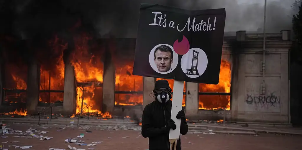 En demonstrant håller upp en bild på president Emmanuel Macron framför en brinnande turistbyrå i Lyon på lördagen.