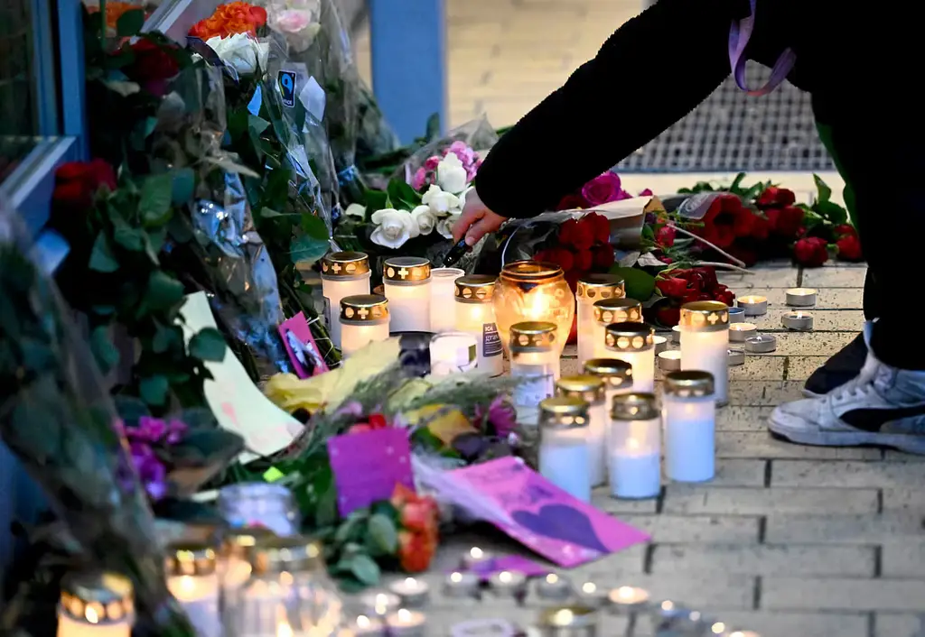 Människor tänder ljus och lämnar blommor vid Kämpetorpshallarna i Solberga i södra Stockholm där en kvinna sköts till döds i fredags.