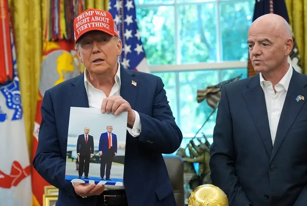 Trump visar upp en bild på honom och Putin. Bredvid honom står Fifas president Gianni Infantino.