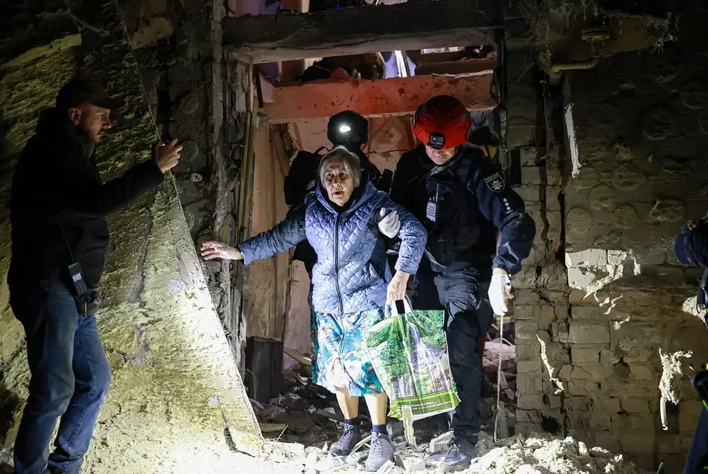 En äldre kvinna leds ut ur ett bombat hus i Zaporizjzja i sydöstra Ukraina.